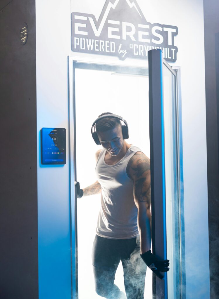 Male exiting cryotherapy chamber for fitness recovery with headphones and fog.