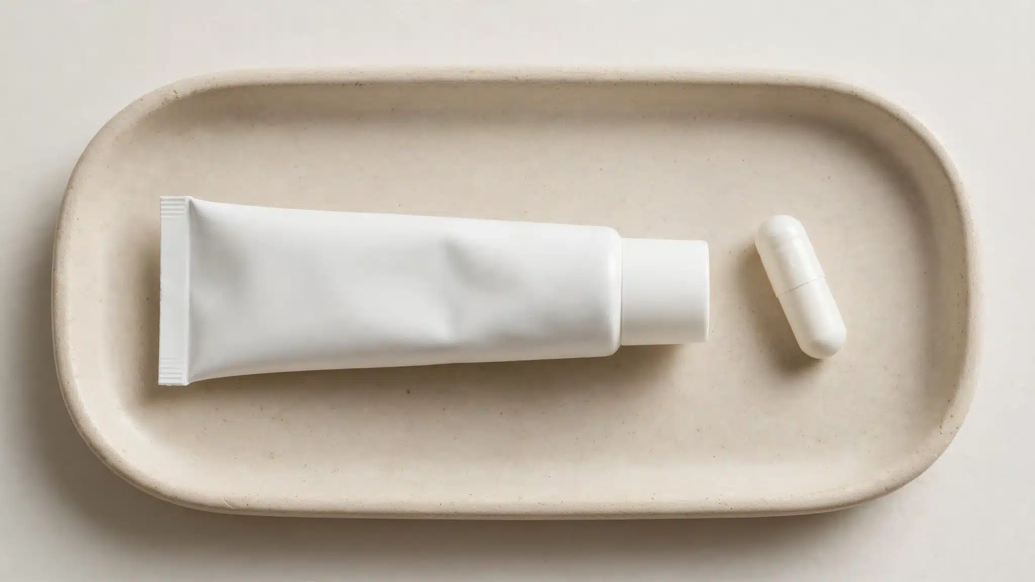 Plain cream tube beside a capsule on a clean surface